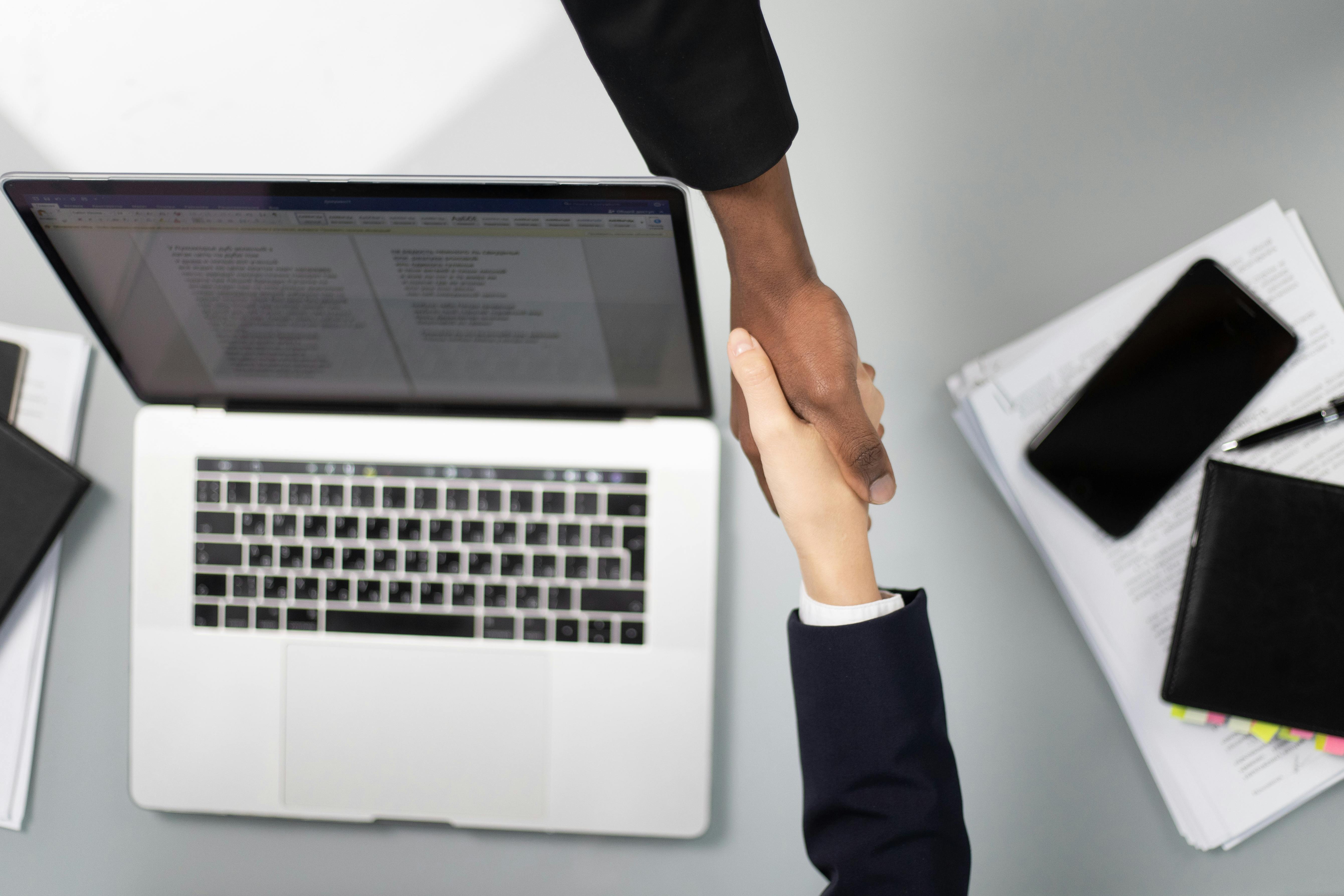 Zwei Personen geben sich über einen Schreibtisch mit Laptop und Unterlagen die Hand. Erfolgreiche KI-Schulungen von Seewald Services GmbH.